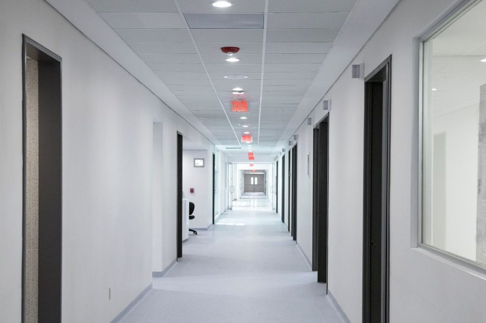 Couloir moderne du cabinet desservant les salles de soins, avec éclairage chaleureux et bois clair.